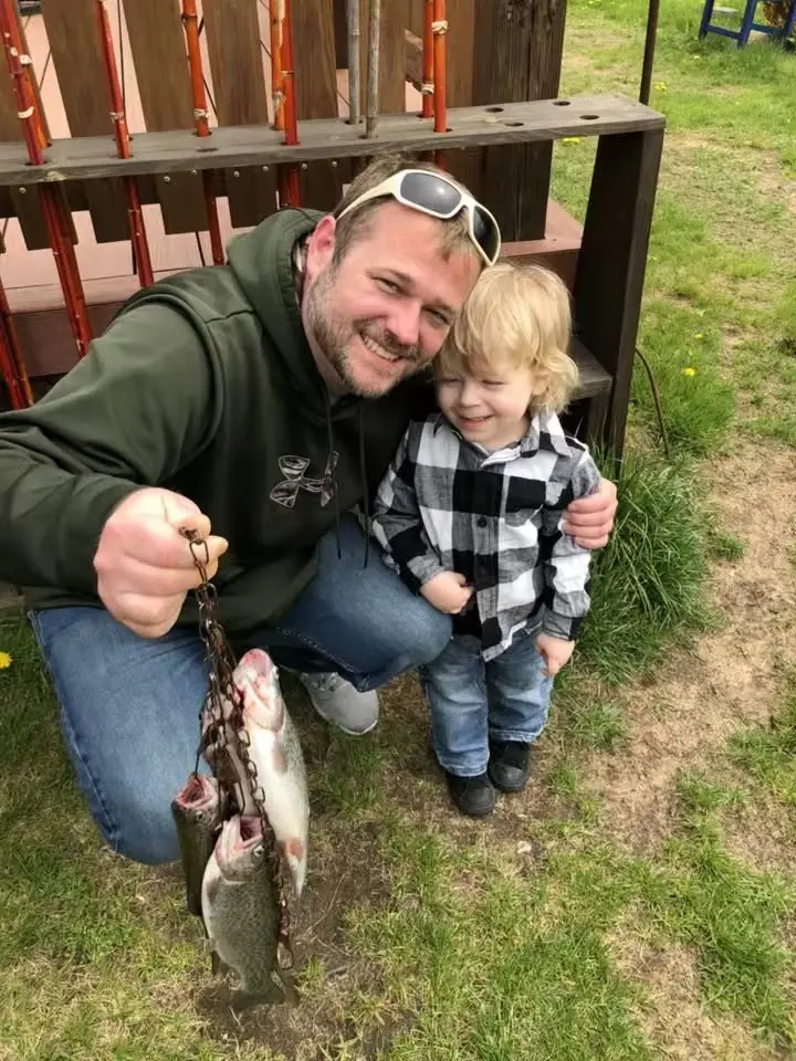 Mike kneeling in a backyard with his young son, holding up a stringer of trout